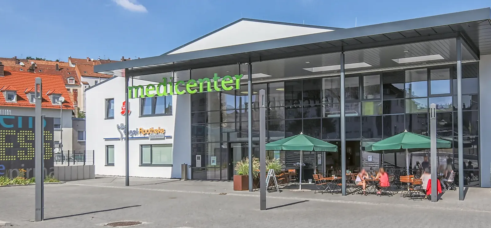 Eingang des medicenter Pirmasens mit Glasfassade, grünem Schriftzug und Außenbereich mit Sonnenschirmen