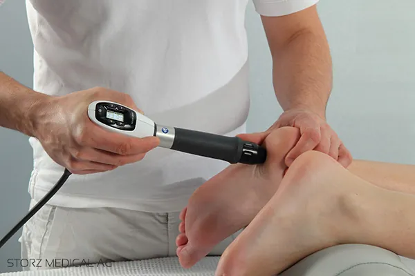 Therapeut behandelt die Fußsohle einer Patientin mit einem Stoßwellen-Handstück